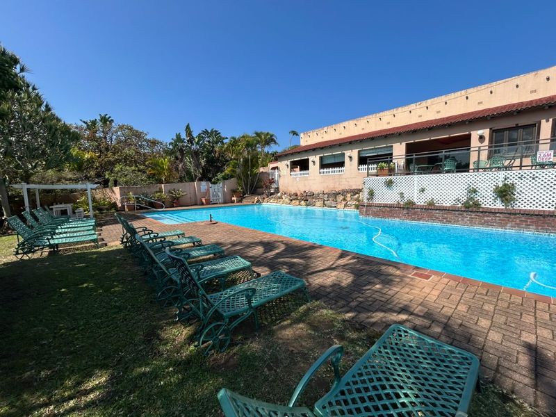 Outdoor pool area featuring a large swimming pool, brick paved surround, retaining wall with lattice fencing, and a pergola structure.