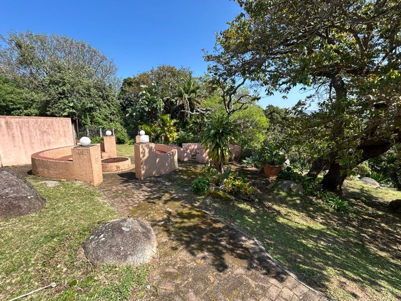 A landscaped garden area featuring a brick-paved pathway, mature trees, and built-in masonry seating structures.