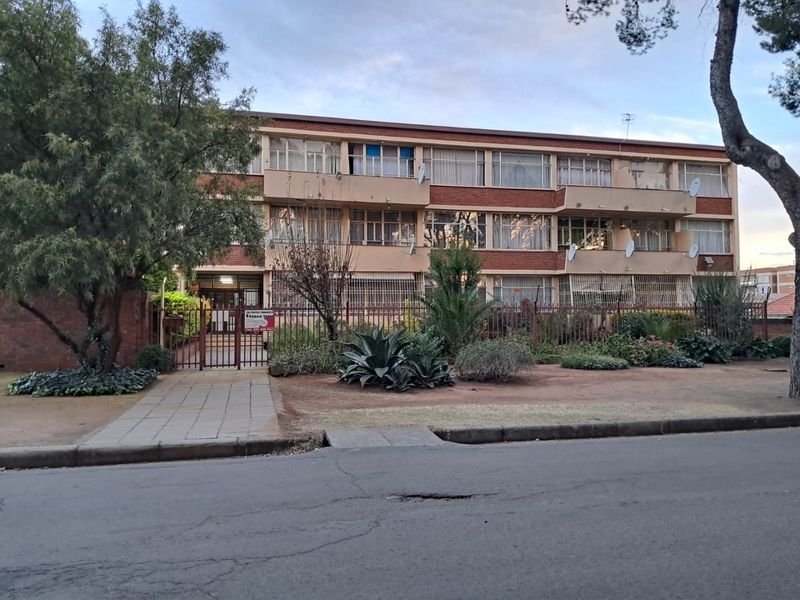 Front view of a multi-story apartment building featuring brick facade, private balconies, and a gated entrance with a paved walkway.
