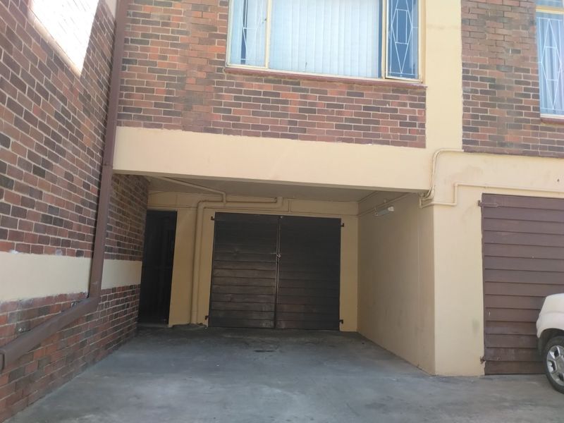 Ground level parking area featuring brick facade, concrete flooring, and double garage doors, showing signs of exterior wear.