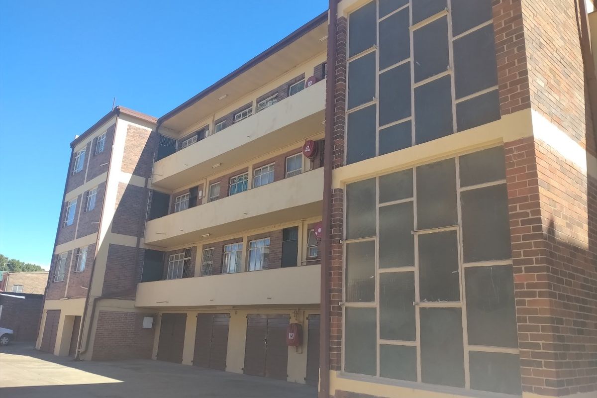 Exterior view of a multi-story apartment building featuring brick facade, multiple levels of balconies, and ground-level garage access.