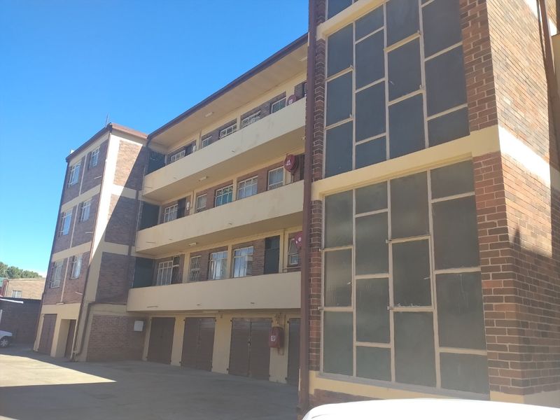 Exterior view of a multi-story apartment building featuring brick facade, multiple levels of balconies, and ground-level garage access.