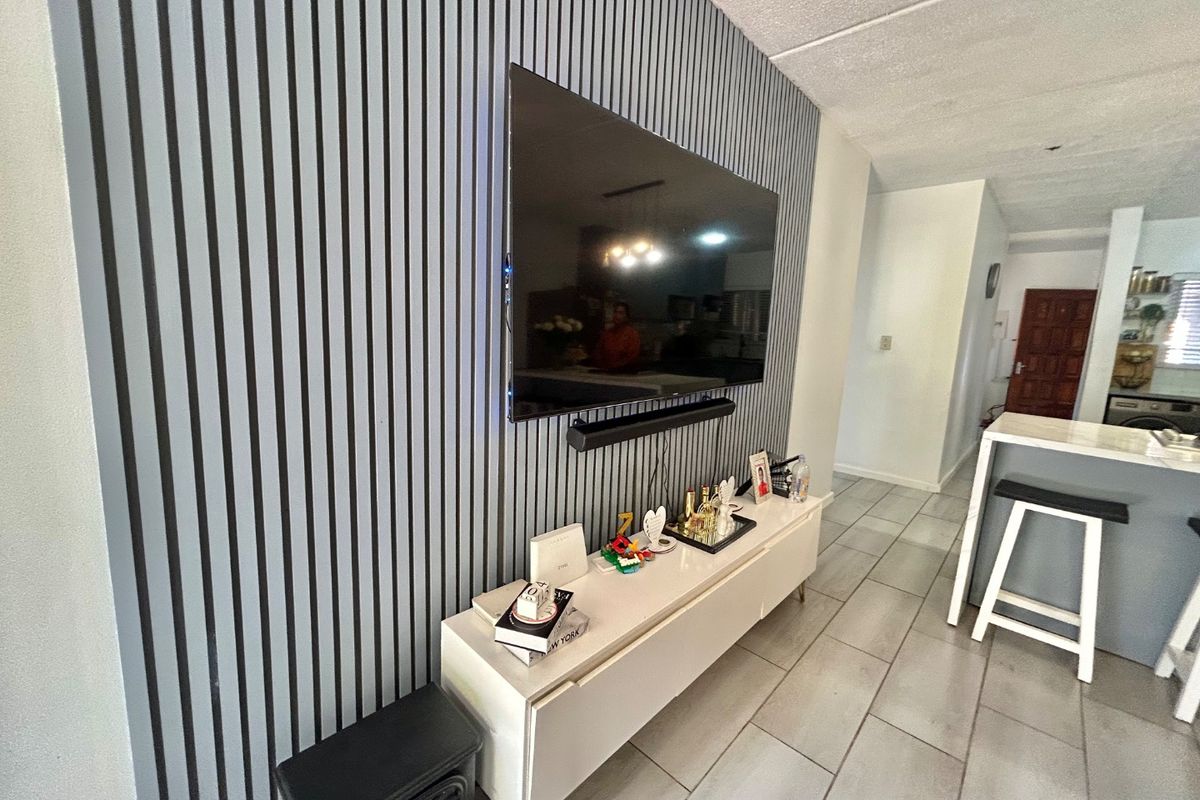A modern living area featuring a contemporary slatted feature wall, tiled flooring, and a wall-mounted television setup.