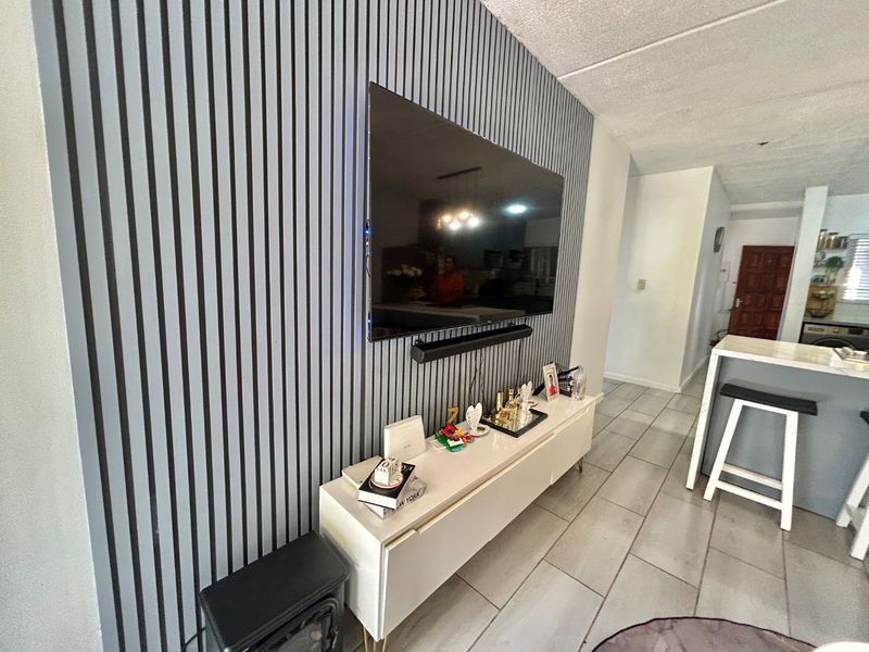 A modern living area featuring a contemporary slatted feature wall, tiled flooring, and a wall-mounted television setup.