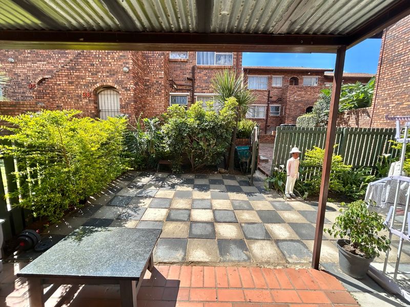 A covered patio area featuring a checkerboard paved floor, brick accents, and direct access to a private garden space.