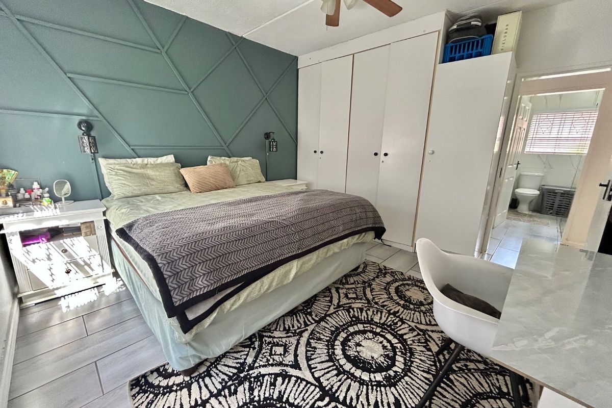 A well-maintained bedroom featuring built-in cupboards, a decorative feature wall, ceiling fan, and tiled flooring, with an adjoining en-suite bathroom.
