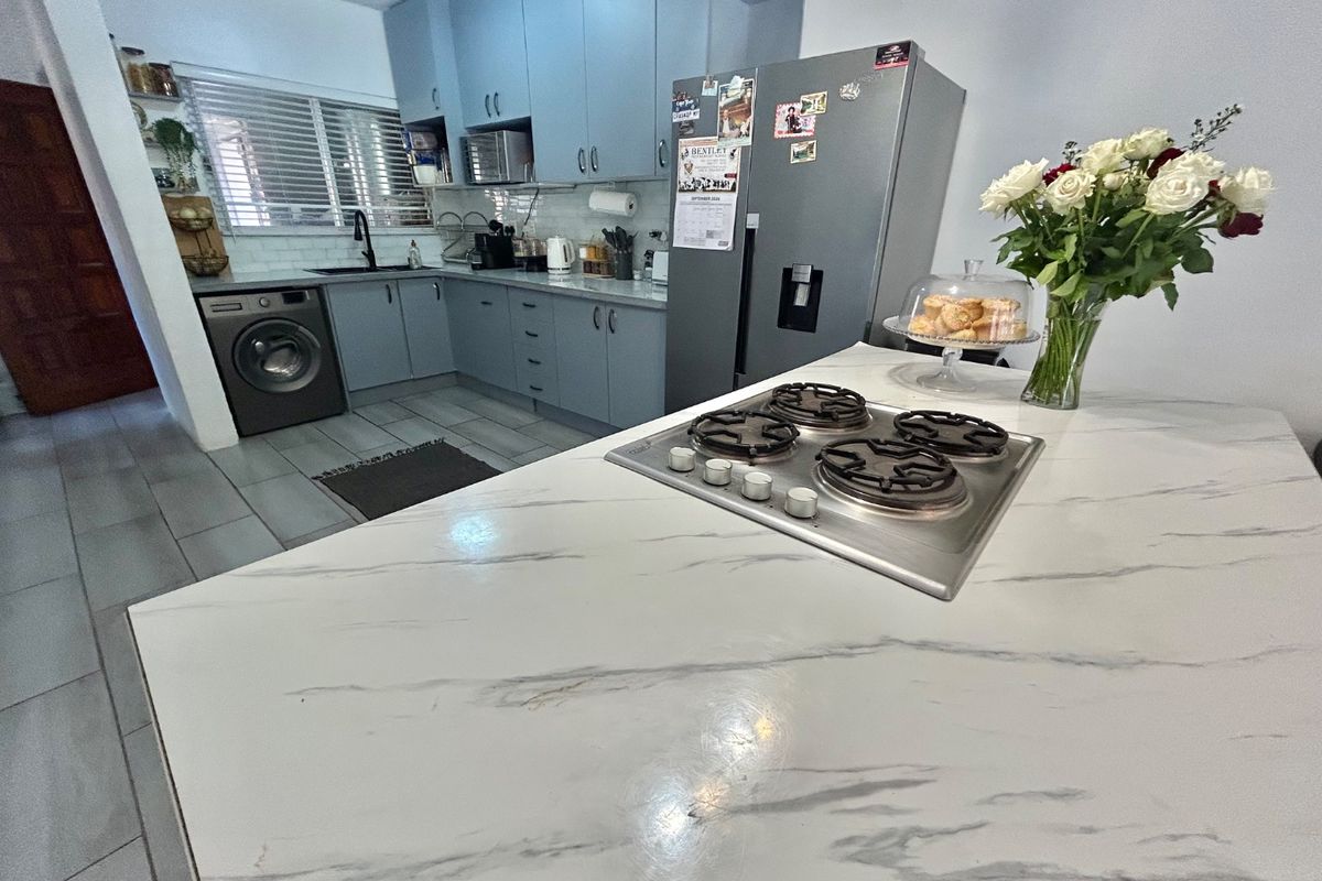 Modern kitchen featuring light blue cabinetry, marble-look countertops, a central island with a gas hob, and integrated laundry appliances.