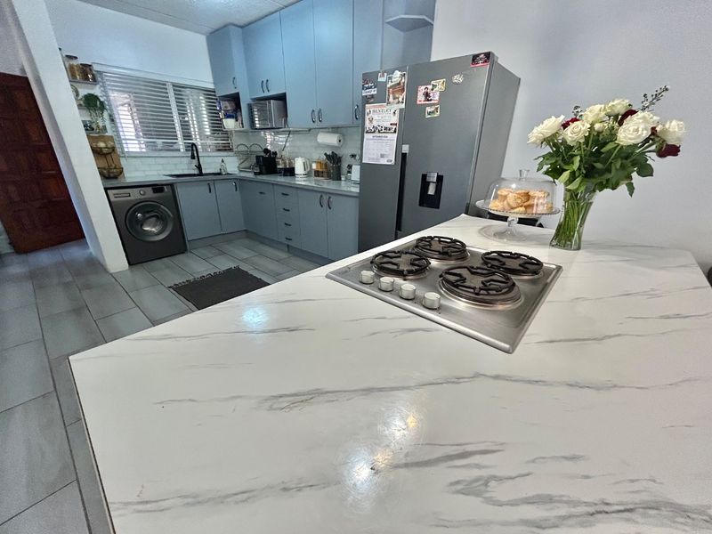 Modern kitchen featuring light blue cabinetry, marble-look countertops, a central island with a gas hob, and integrated laundry appliances.