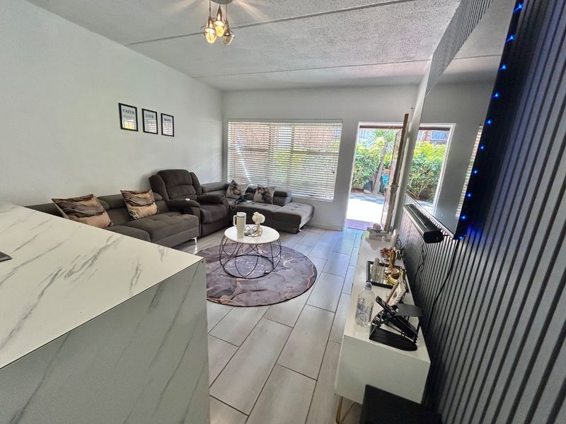 A bright living room featuring tiled flooring, a textured ceiling, and a modern feature wall, with direct access to an outdoor patio area.