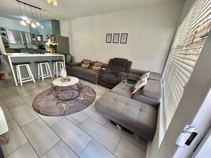 Open-plan living area featuring a modern kitchen with a central island, tiled flooring, and large windows with fitted venetian blinds.