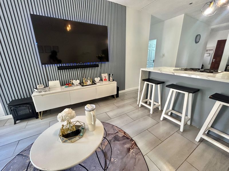 Modern open-plan living area featuring a stylish slatted feature wall, marble-look breakfast bar with integrated hob, and contemporary ceramic floor tiling.