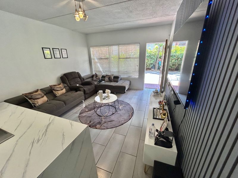 A well-maintained living room featuring tiled flooring, decorative wall paneling, and direct access to an outdoor patio area.