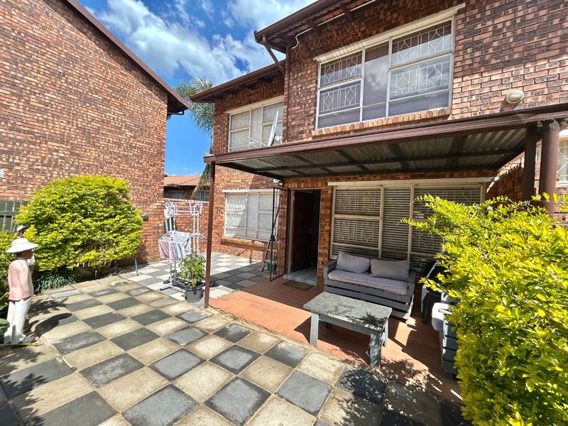 Rear exterior view of the townhouse featuring a brick facade, a covered patio area, and a paved courtyard space.