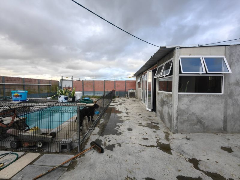 Outdoor pool area featuring a concrete patio, perimeter wall with electric fencing, and an exterior structure with aluminium windows and sliding doors.