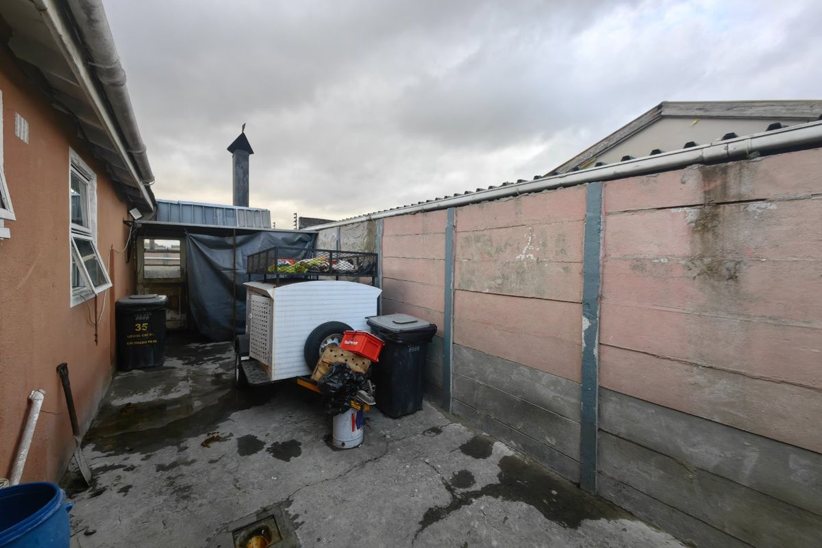 A rear exterior utility area featuring concrete paving and a boundary wall, requiring maintenance and general cleanup to improve the outdoor space.
