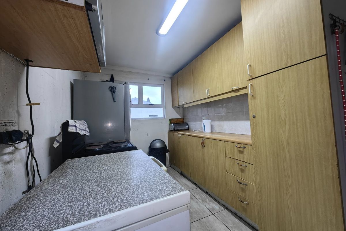 A functional kitchen featuring laminate cabinetry, tiled backsplash, and tiled flooring, currently requiring cosmetic updates and improved finishings.