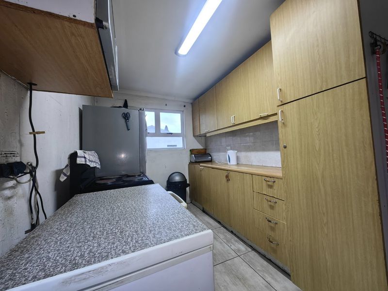 A functional kitchen featuring laminate cabinetry, tiled backsplash, and tiled flooring, currently requiring cosmetic updates and improved finishings.