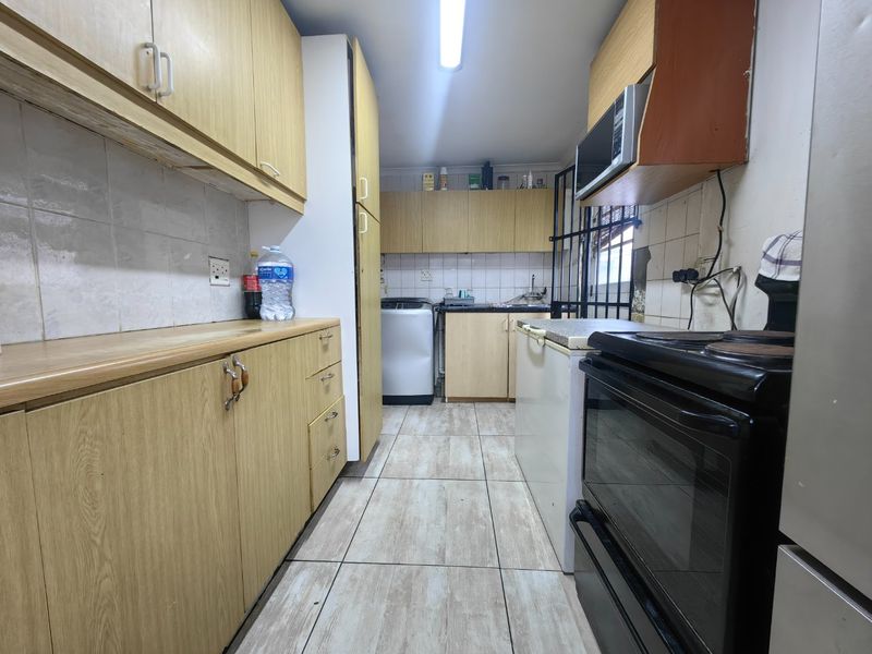 A functional kitchen featuring laminate cabinetry, tiled backsplash, and built-in appliances, offering a practical layout with potential for cosmetic updates.