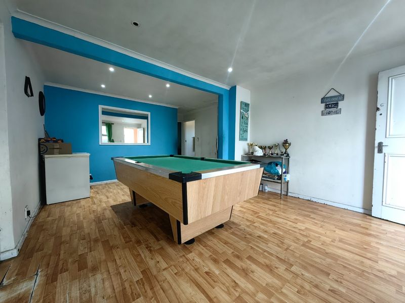 A multi-purpose living area featuring laminate flooring, recessed downlighting, and a bright blue accent wall, offering a versatile space for recreation or relaxation.