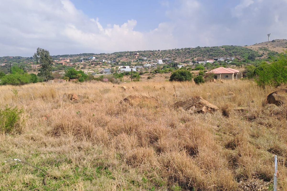 A wide-angle view of an undeveloped plot of land with natural vegetation, rocky outcrops, and surrounding residential hillside landscape.