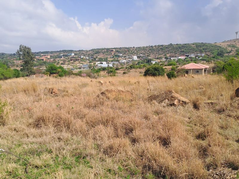 A wide-angle view of an undeveloped plot of land with natural vegetation, rocky outcrops, and surrounding residential hillside landscape.