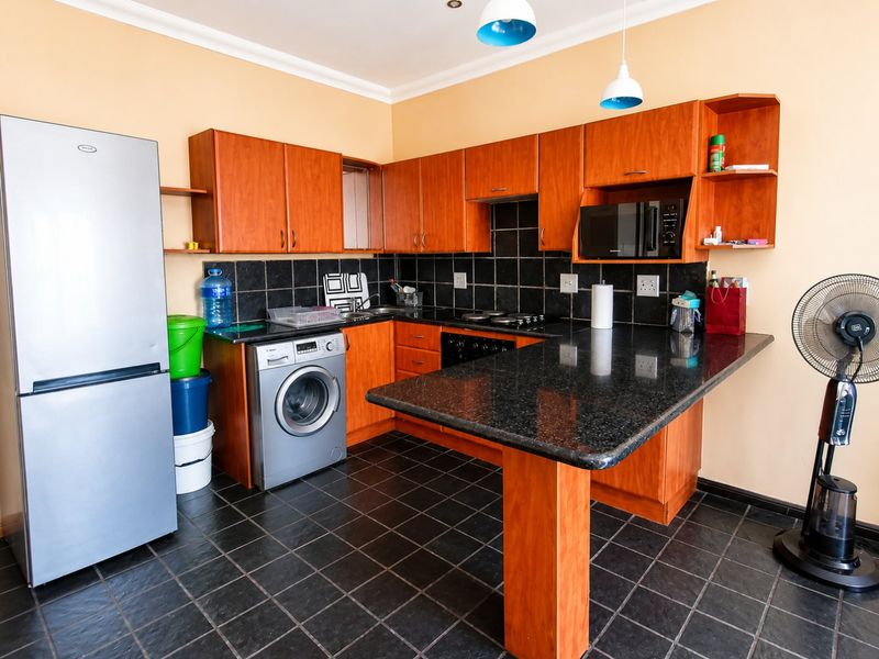 A functional kitchen featuring wooden cabinetry, granite countertops, a breakfast bar, and a black tiled backsplash with built-in appliances.