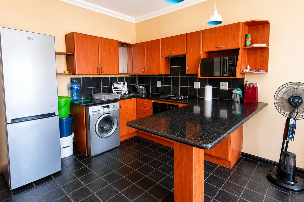 A functional kitchen featuring wooden cabinetry, granite countertops, a breakfast bar, and a black tiled backsplash with built-in appliances.
