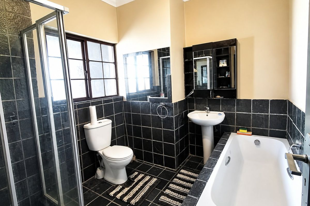 A functional bathroom featuring a pedestal basin, built-in bathtub, separate shower enclosure, and dark tiled finishes throughout.