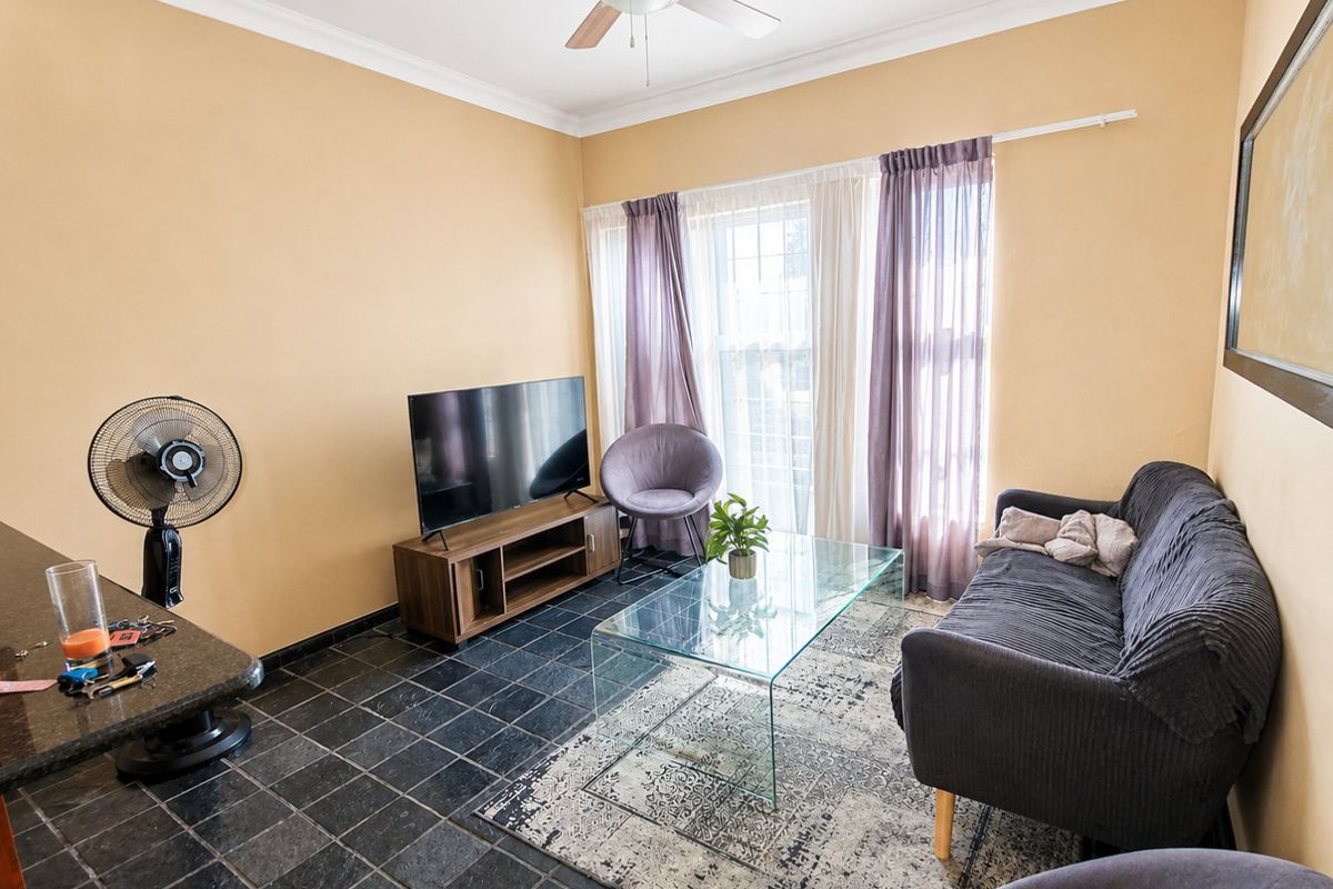 A living room featuring dark tiled flooring, a ceiling fan, and coved cornicing, providing a functional space with natural light from the window.