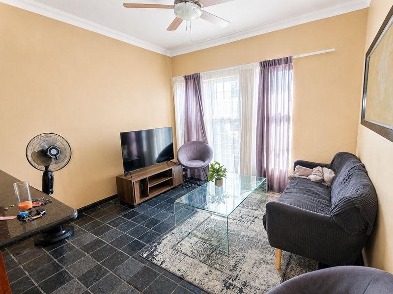 A living room featuring dark tiled flooring, a ceiling fan, and coved cornicing, providing a functional space with natural light from the window.