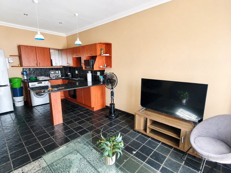 Open-plan living area featuring a kitchen with wood-finish cabinetry, granite countertops, and dark tiled flooring throughout the combined space.