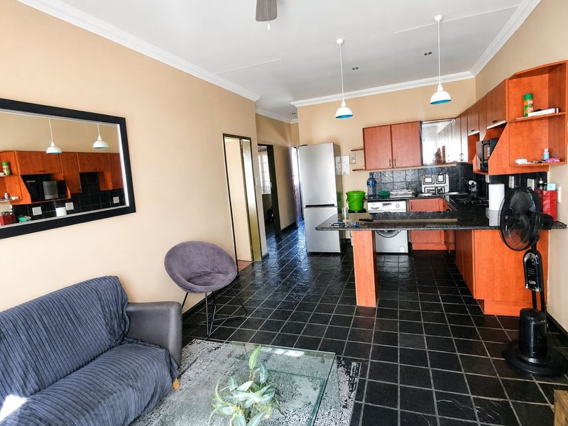 Open-plan living and kitchen area featuring dark tiled flooring, wooden cabinetry, granite countertops, and pendant lighting in a functional, lived-in apartment layout.