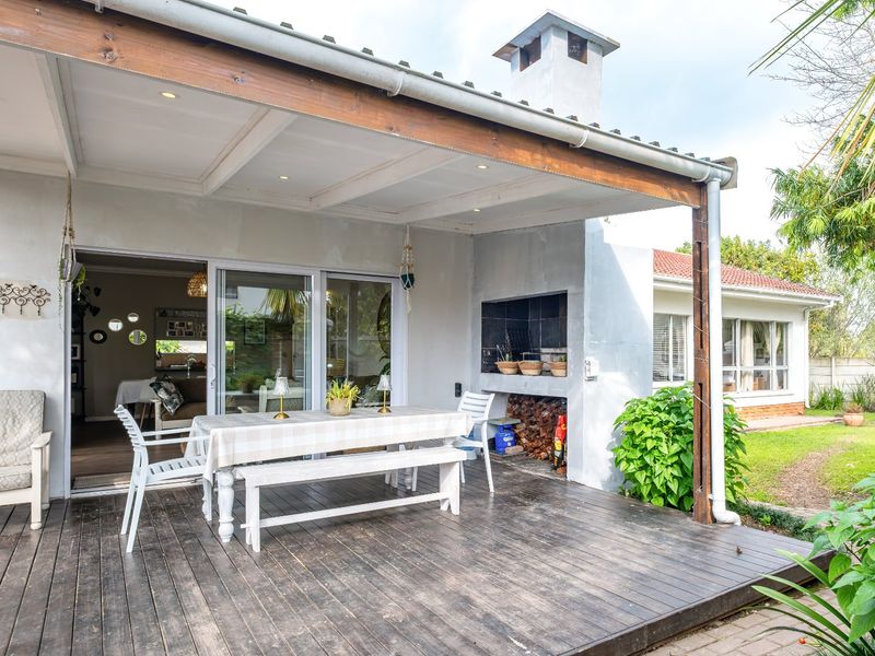 Covered outdoor patio featuring timber decking, a built-in braai, and direct access to the interior living space through sliding glass doors.