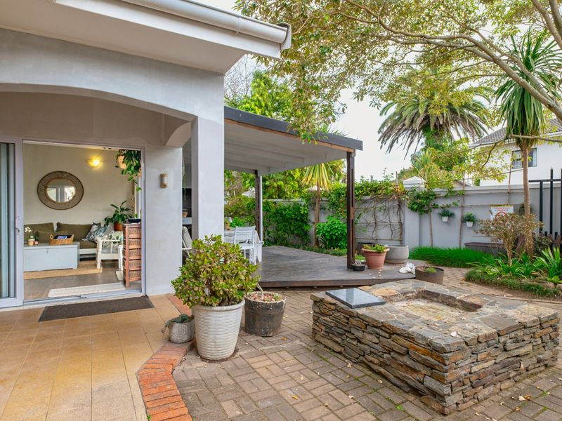 Rear garden area featuring a paved courtyard with a stone fire pit, timber decking, and a covered patio leading into the living space.