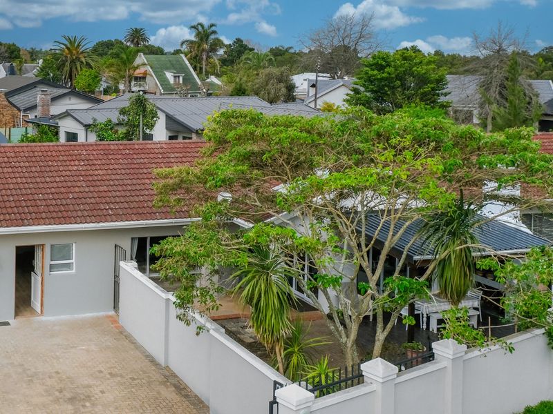 Aerial view of the property showing the tiled roof, paved driveway, boundary wall, and covered patio area within a residential neighbourhood.