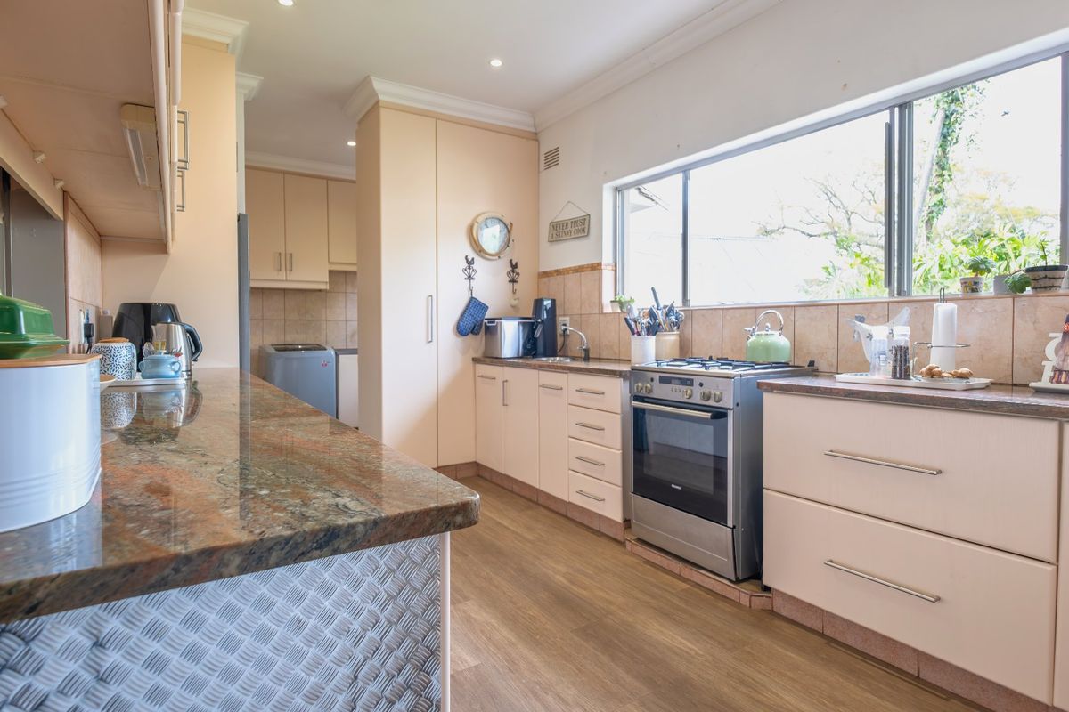 A functional kitchen featuring granite countertops, ample built-in cabinetry, a tiled backsplash, and a large window providing natural light.