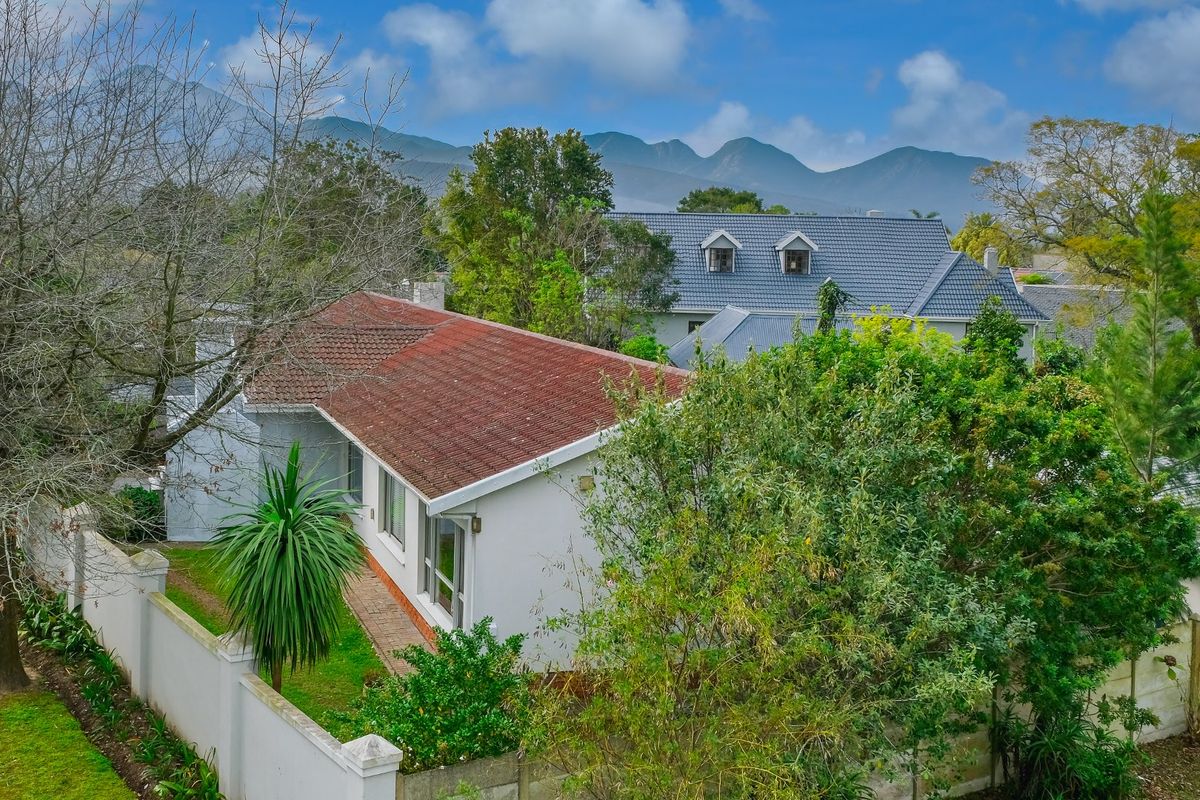 Aerial view of the property showing the roof structure, surrounding garden, and boundary walls with mountain views in the background.