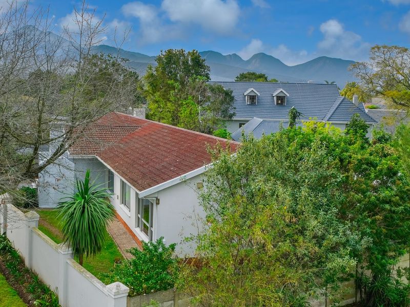 Aerial view of the property showing the roof structure, surrounding garden, and boundary walls with mountain views in the background.
