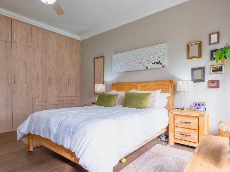A well-maintained bedroom featuring extensive built-in wooden cabinetry, laminate flooring, and a ceiling fan, offering a clean and functional living space.