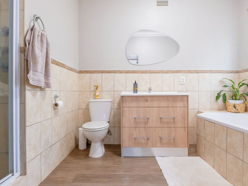 A well-maintained bathroom featuring a modern wood-finish vanity, a separate shower enclosure, a bathtub, and neutral wall tiling.