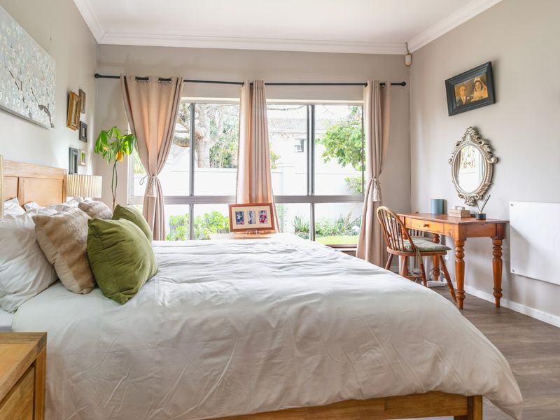 A well-lit bedroom featuring large windows, laminate flooring, and a wall-mounted heater, offering a comfortable and functional living space.