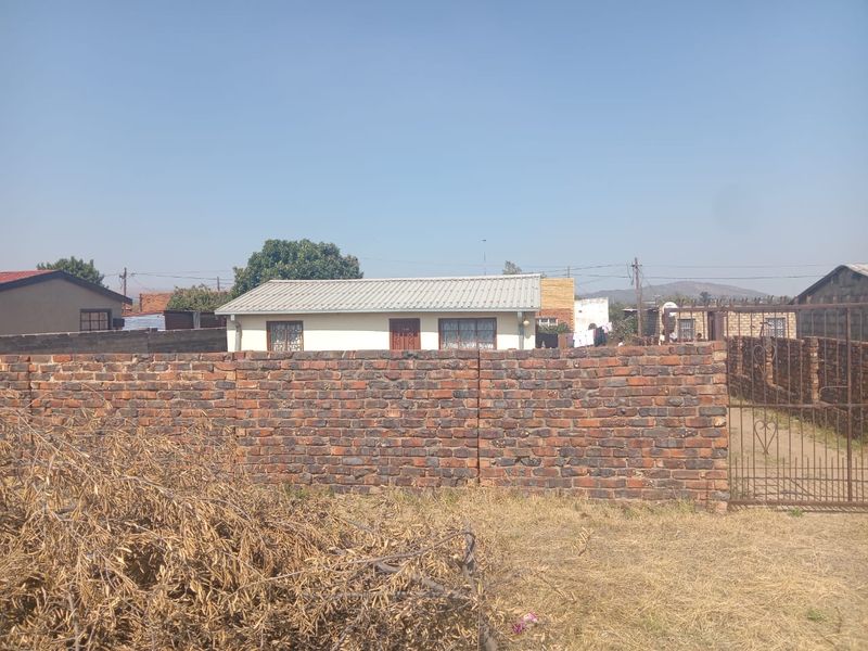 Front view of a residential property featuring a brick boundary wall, metal gate, and a structure with a corrugated metal roof.