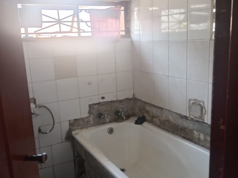 A small bathroom featuring a bathtub with significant wall tile damage and exposed substrate, requiring renovation and repair of the wall finishes.