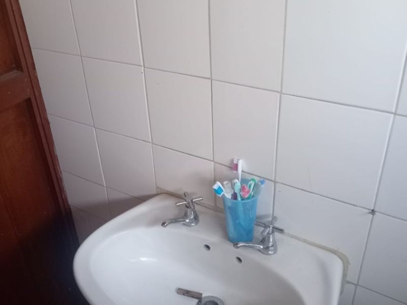 A functional bathroom washbasin area featuring a pedestal sink and tiled walls, showing signs of wear and requiring minor maintenance.