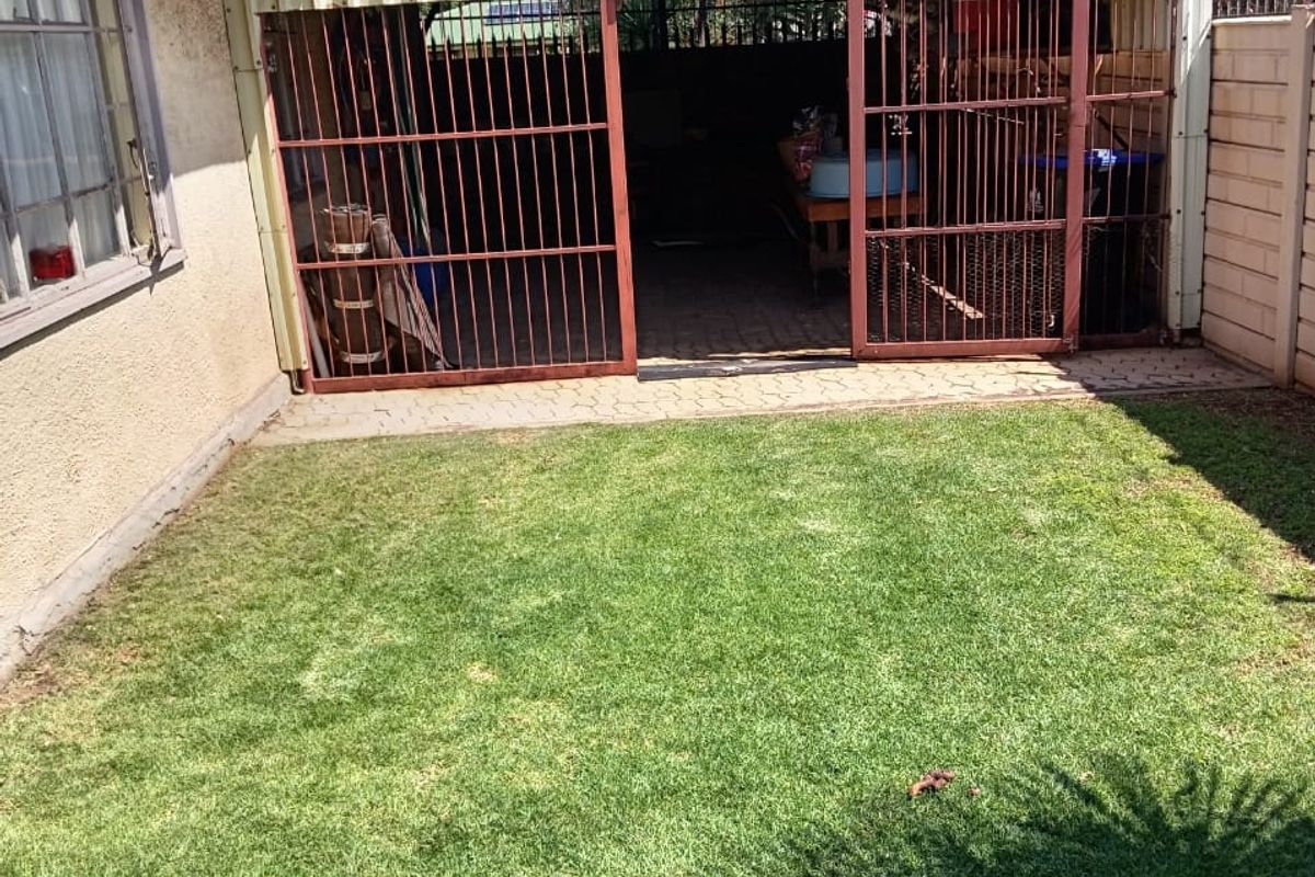 Rear garden area featuring a lawn, paved patio, and a covered storage or utility space enclosed by security gates.