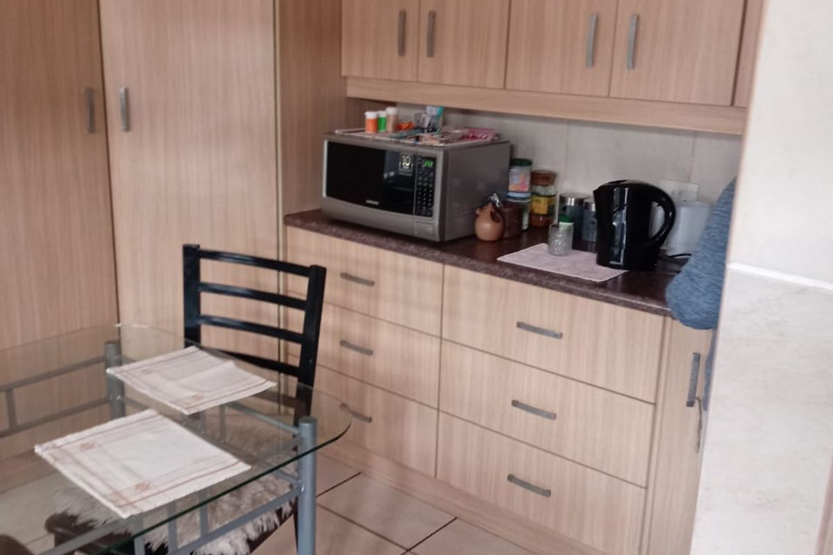 A functional kitchen area featuring light wood-tone laminate cabinetry, matching countertops, and ceramic floor tiles.
