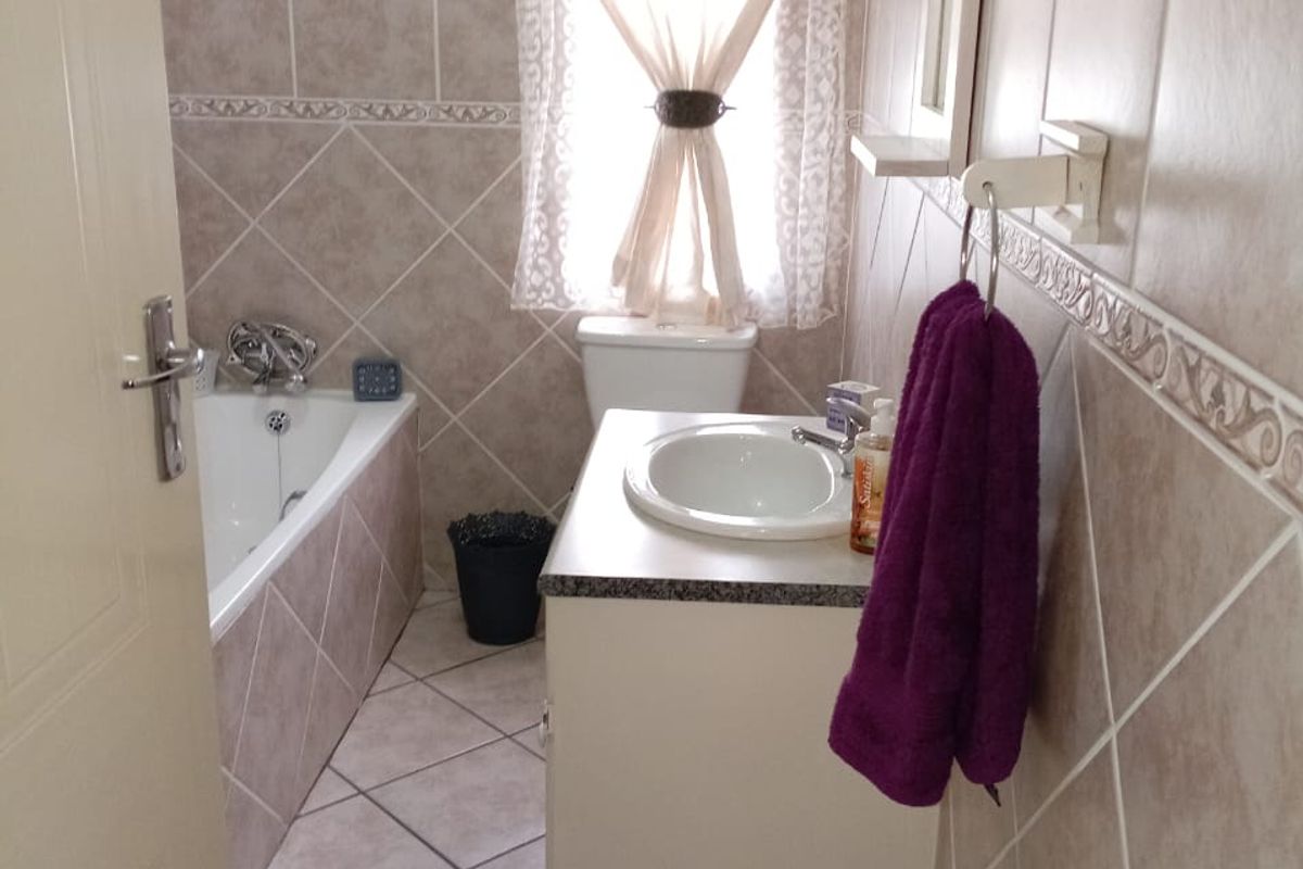 A functional bathroom featuring tiled walls and floors, a built-in bathtub, a vanity cabinet with a basin, and a toilet.