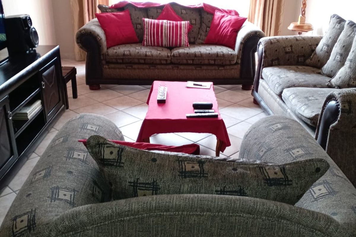 A comfortable living room featuring tiled flooring and large windows with curtain rails, providing a bright and functional space.