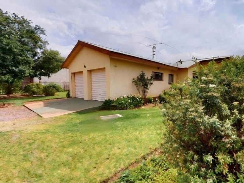 Front view of a residential property featuring a double garage with roll-up doors, set within a well-maintained garden area.