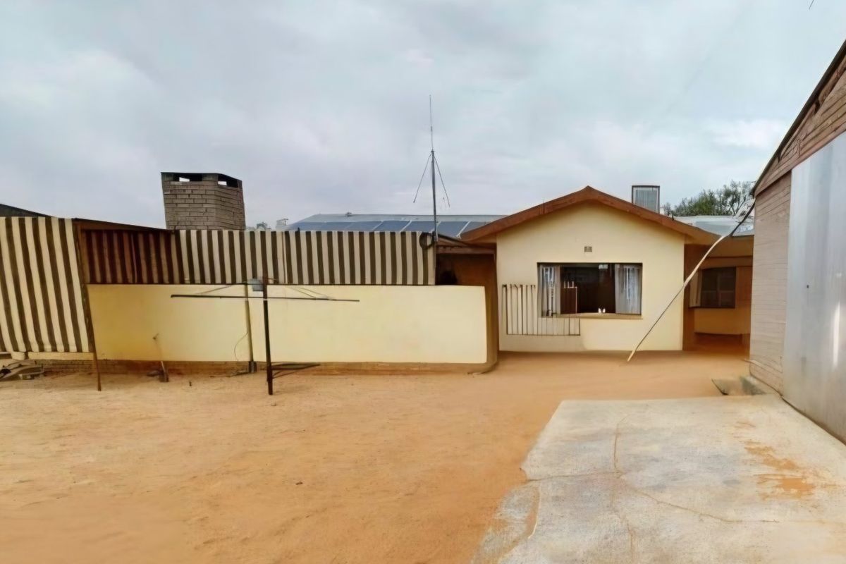 Rear view of the property featuring a sandy yard, boundary wall, solar panels, and a brick chimney.